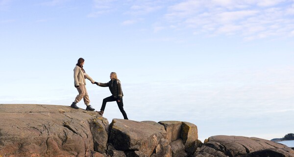 Two women on a cliff next to ocean, holding hands.