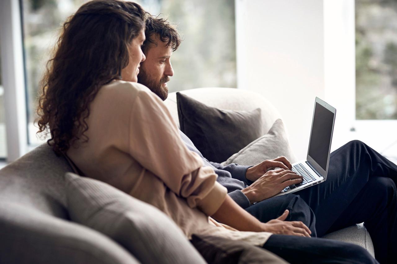 En man och en kvinna sitter nära varandra i en soffa och kollar på en laptop tillsammans