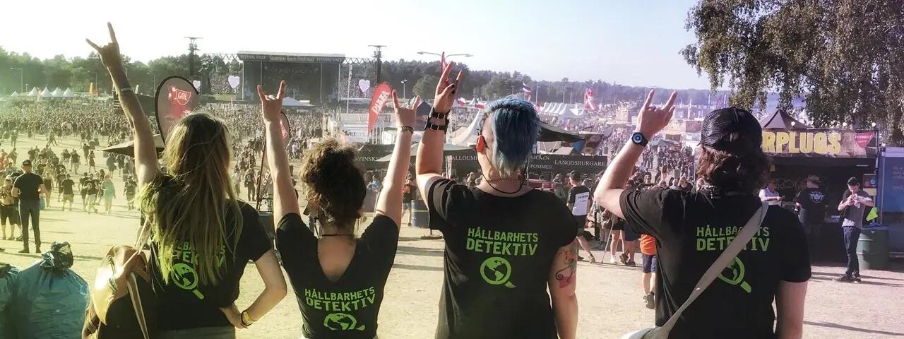 Två kvinnor och två män med utsikt över scenområdet på en festival med t-shirts där det står "hållbarhetsdetektiv"