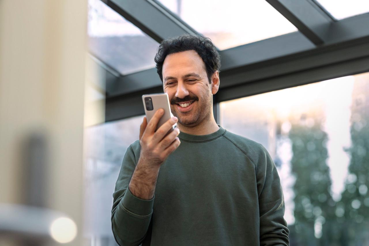 Man med mustasch tittar i sin telefon och ler stort