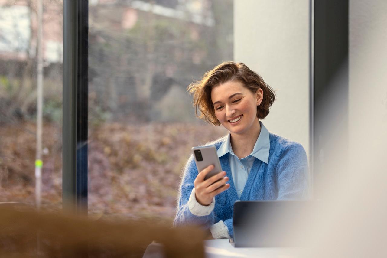 Kvinna sitter vid köksbord och tittar på sin telefon